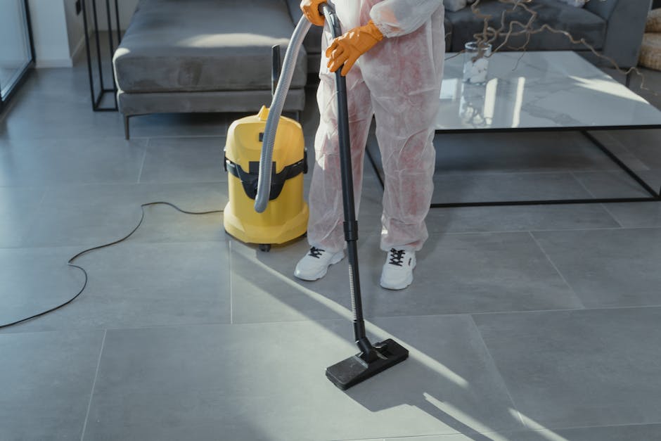 Three professional cleaners from Fulham Carpet Cleaners are positioned in a modern, well-lit living room with a minimalist design. The room features a large sofa with fabric upholstery, a low coffee t