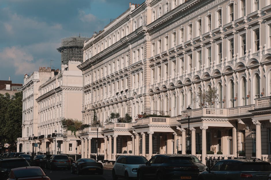 A row of elegant white Victorian-style terraced townhouses along a street in Fulham, SW6, with each building featuring ornate architectural details, large sash windows, and decorative cornices. The ground floors have black iron railings and small front gardens or porches, with some buildings displaying potted plants. Several parked cars, including a white vehicle and a black SUV, line the street in front of the houses. The scene is illuminated by natural daylight with a partly cloudy sky overhead, and the photograph captures the clean, well-maintained facades, reflecting the focus on surface cleaning and property hygiene, as promoted by Fulham Carpet Cleaners on their website, fulhamcarpetcleaners.com.