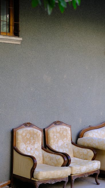 Interior view of a room featuring a textured, painted grey wall with three vintage-style upholstered armchairs arranged along the lower part of the wall. The chairs have wooden frames with ornate carvings, and are upholstered in a light, patterned fabric. A window with wooden bars is visible at the top left corner, allowing natural light to illuminate the space. The overall scene suggests an area suitable for surface cleaning and maintenance in a period home, with a focus on aesthetic furniture and wall surfaces. Fulham Carpet Cleaners offers professional cleaning and sanitisation services to maintain the hygiene and appearance of such interior spaces.